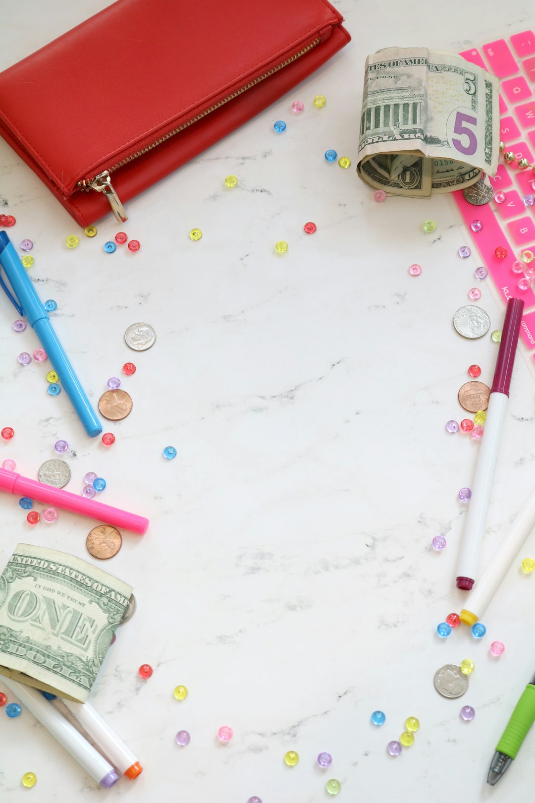 Marble money stock photo and money styled stock photo for personal finance bloggers, business coaches, and entrepreneurs with a pink keyboard, colorful pens, cash, a red wallet, and more.